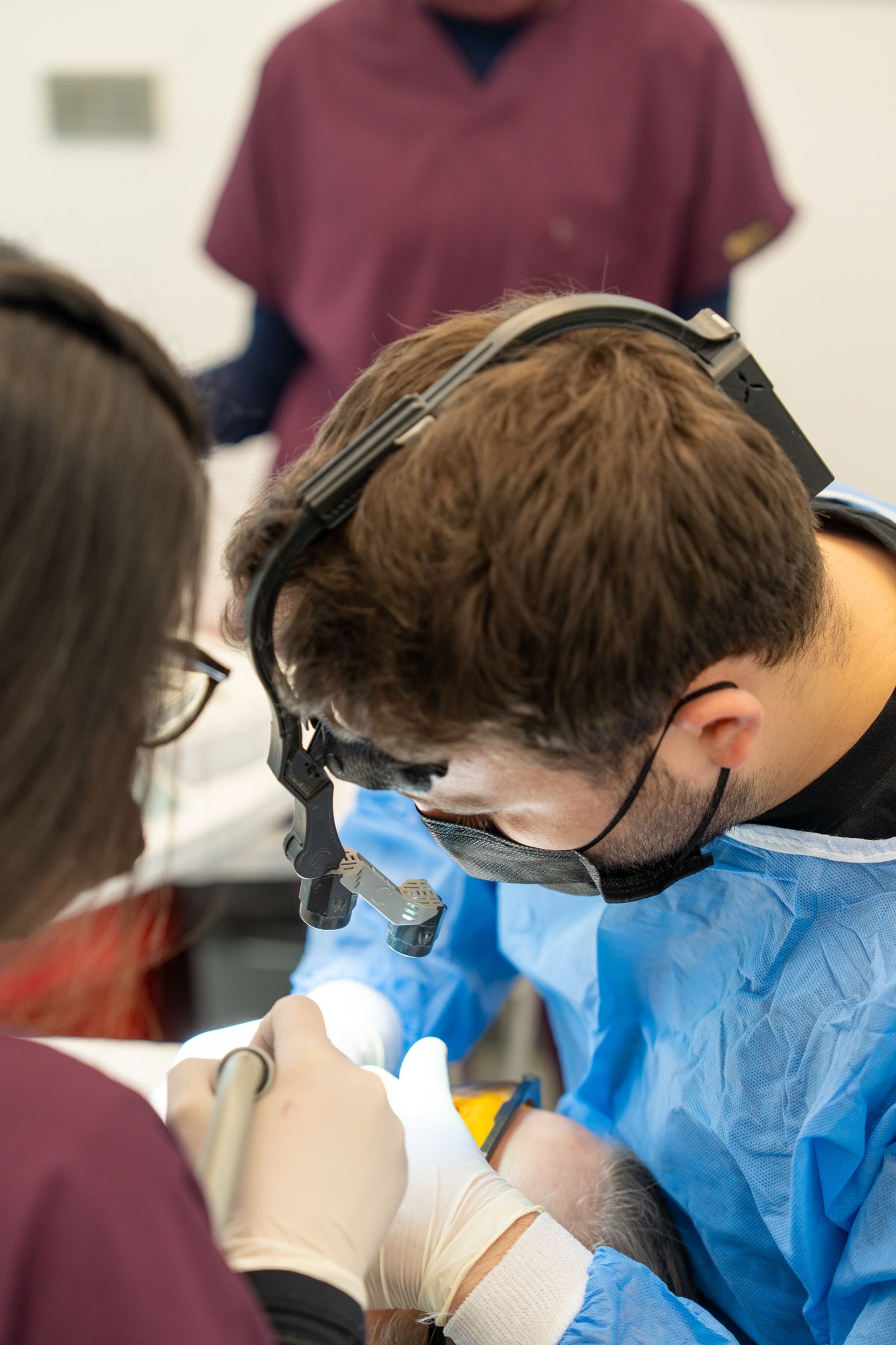 A dentist in a surgical gown at work, supported by the team.
