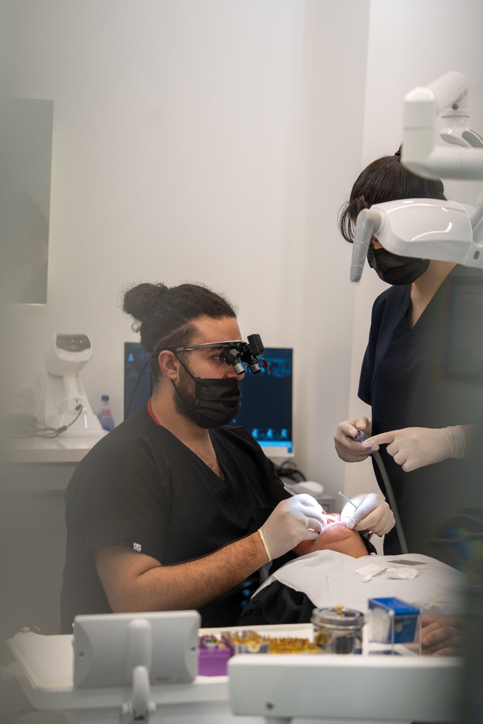 A dentist treating a patient, assisted by a team member.