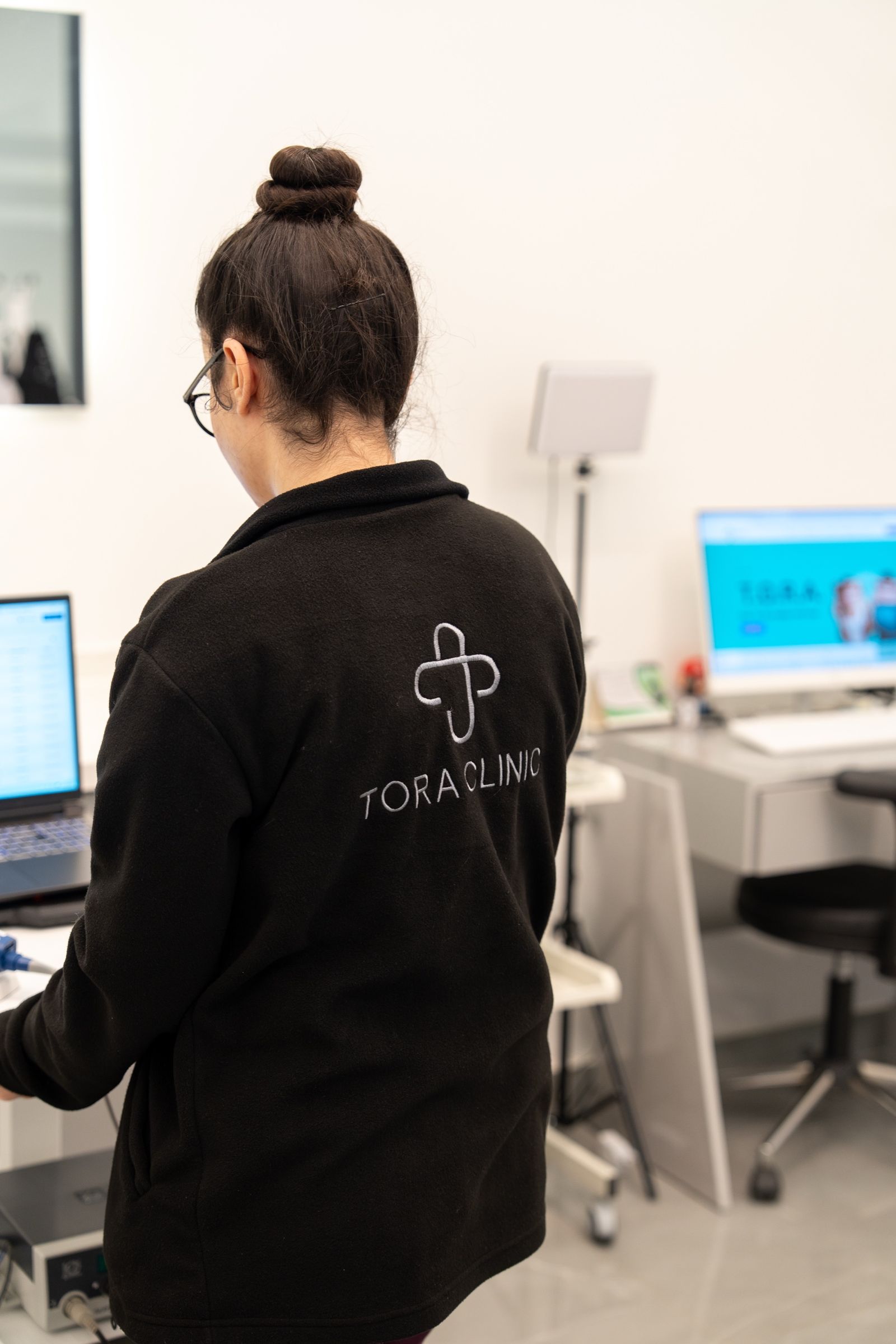 A team member in a TORA Clinic jacket working at a computer.