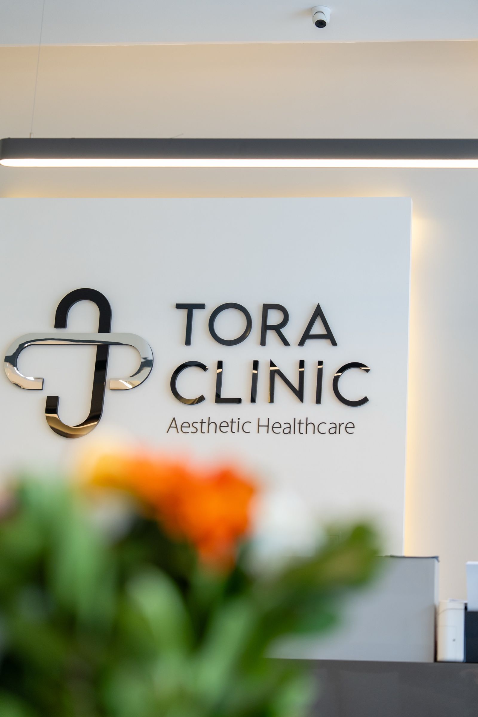 The TORA Clinic logo on the reception wall, behind flowers.