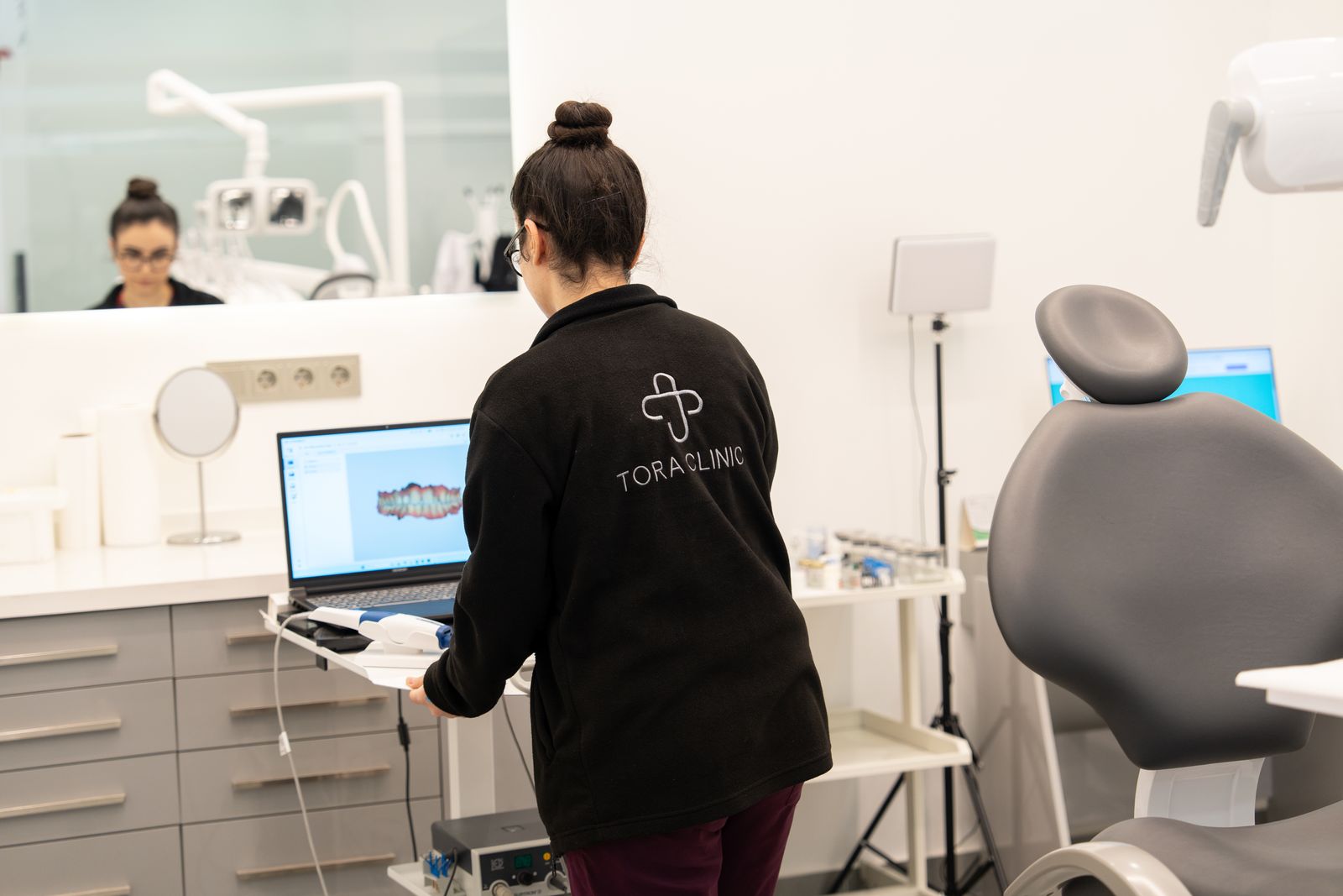 A TORA Clinic team member reviewing a digital intraoral scan on a laptop beside a treatment chair.